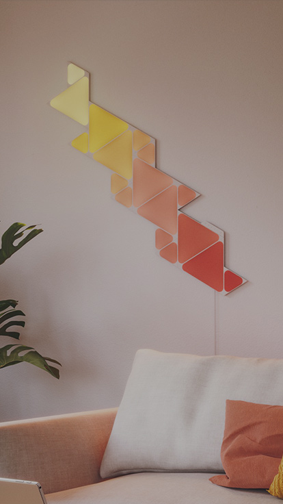 This is an image of Nanoleaf Shapes Triangles and Mini Triangles on the wall above the couch in a living room. The modular color changing smart light panels are connected together with linkers and have over 16 million colors.