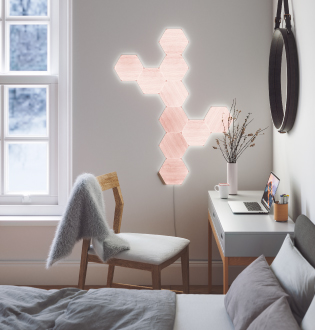 This is an image of a 10 panel Nanoleaf Elements layout mounted onto the wall beside a desk in a bedroom. These smart light panels create geometric wall art that illuminates with a dynamic glow. Modular smart lights are connected together with linkers and are perfect for small spaces.